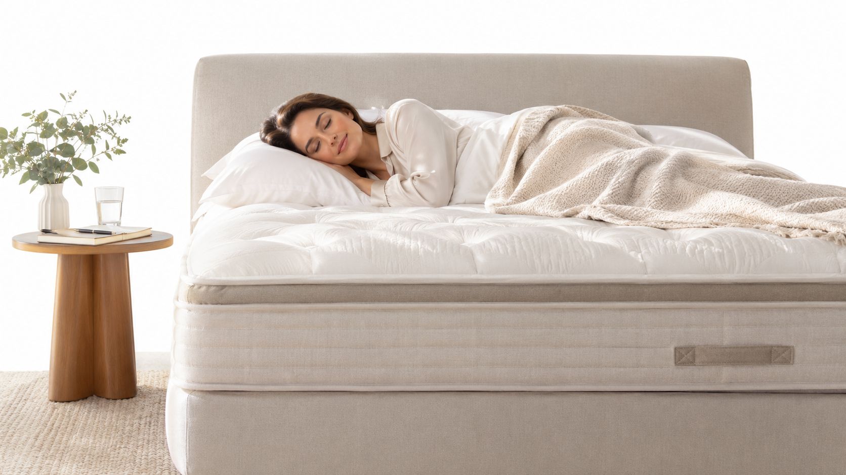 A woman sleeping comfortably on a high-end luxury mattress in a modern, neutral-toned bedroom setting.